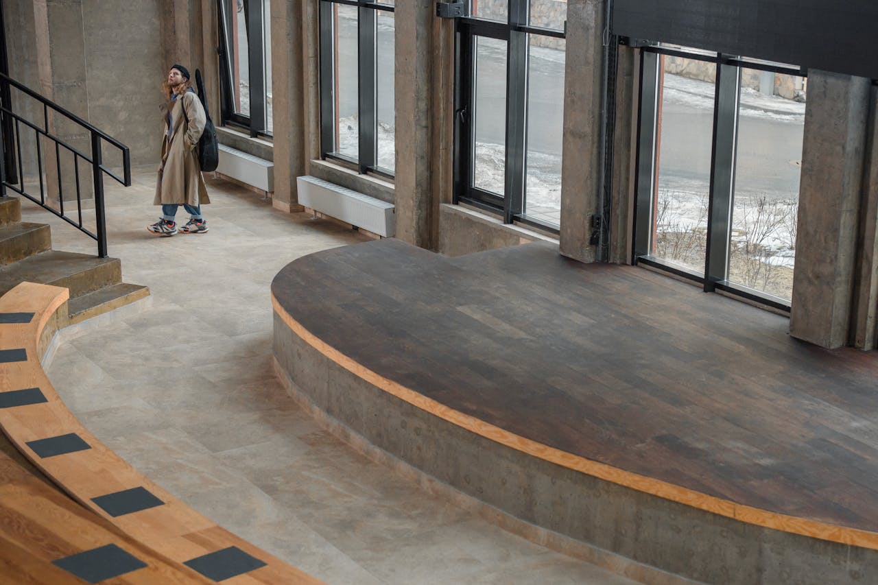 A modern amphitheater with large windows and a lone person in a trench coat, indoors.